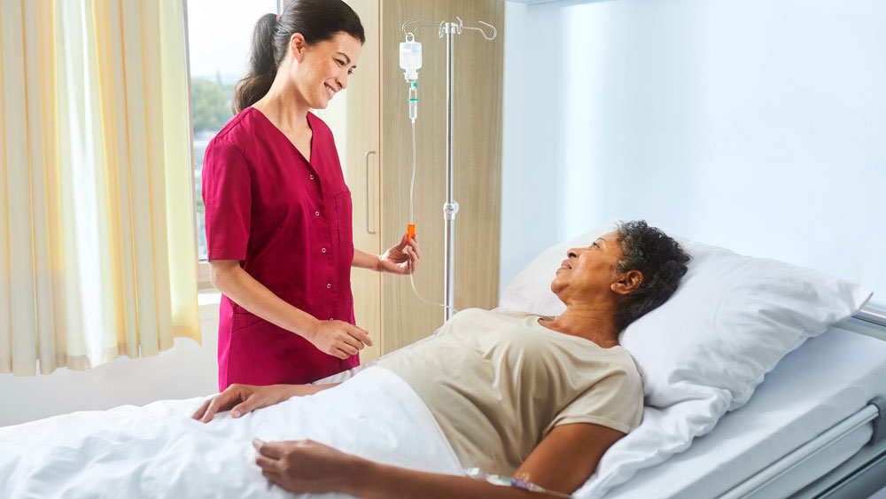 Enfermera con ecoflac plus en un soporte de infusión hablando con un paciente tumbado en la cama