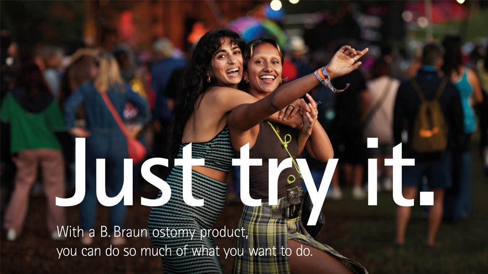 Two girls dancing at an outdoor music festival with a crowd and stage in the background. The text on the image reads Just try it. With a B. Braun ostomy product, you can do so much of what you want to.