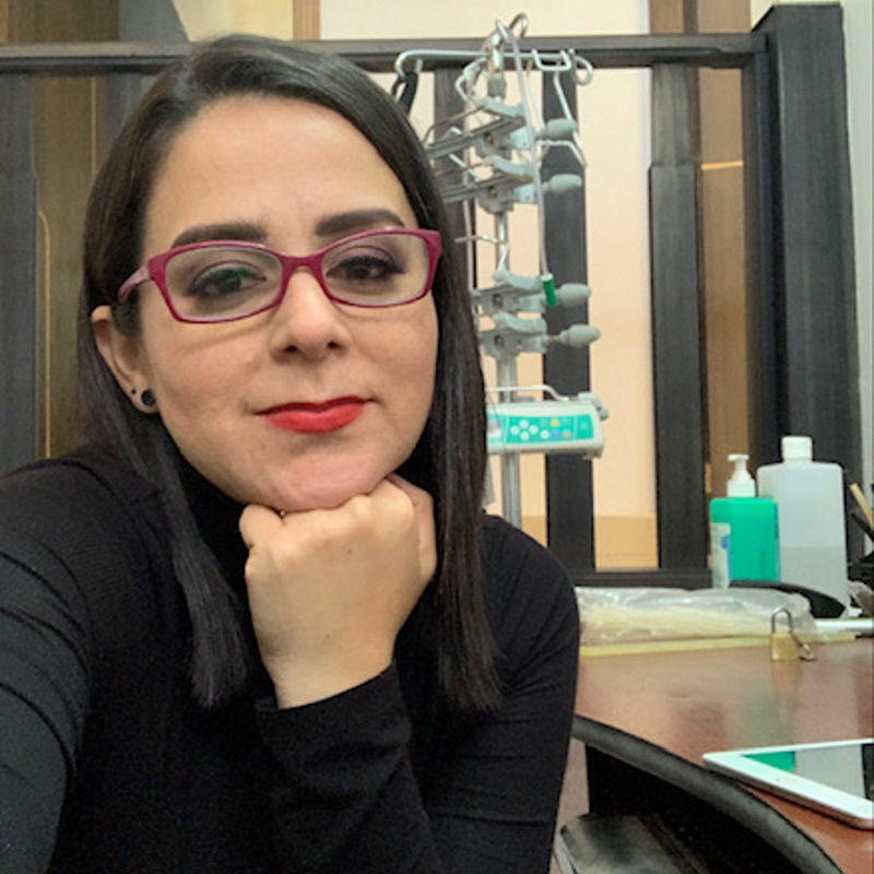 mujer con cabello oscuro, gafas y barra de labios descansando la cabeza sobre su mano