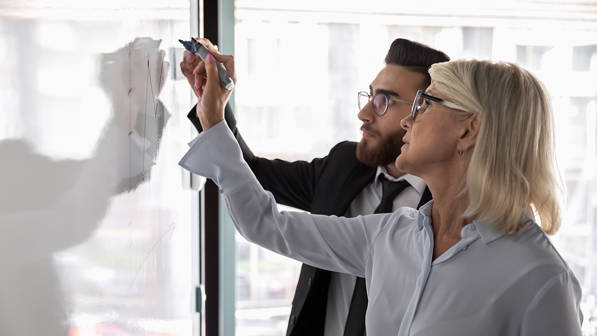 Personas empresariales diversas y concentradas que escriben en una pizarra y participan en el pensamiento creativo juntos, compañeros multirraciales centrados que hacen una lluvia de ideas y desarrollan estrategias empresariales en un rotafolio, concepto de trabajo en equipo
