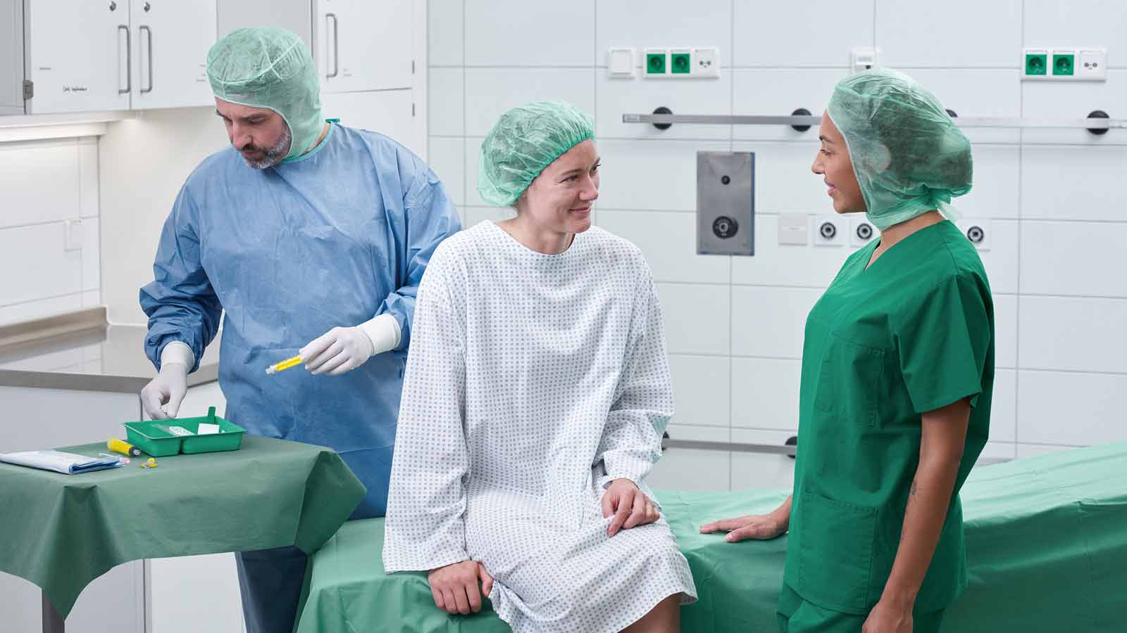 Habitación de hospital con equipo médico, que muestra una cama de paciente, dispositivos de monitorización y suministros clínicos. Un profesional sanitario con ropa médica se está preparando para la atención al paciente.
