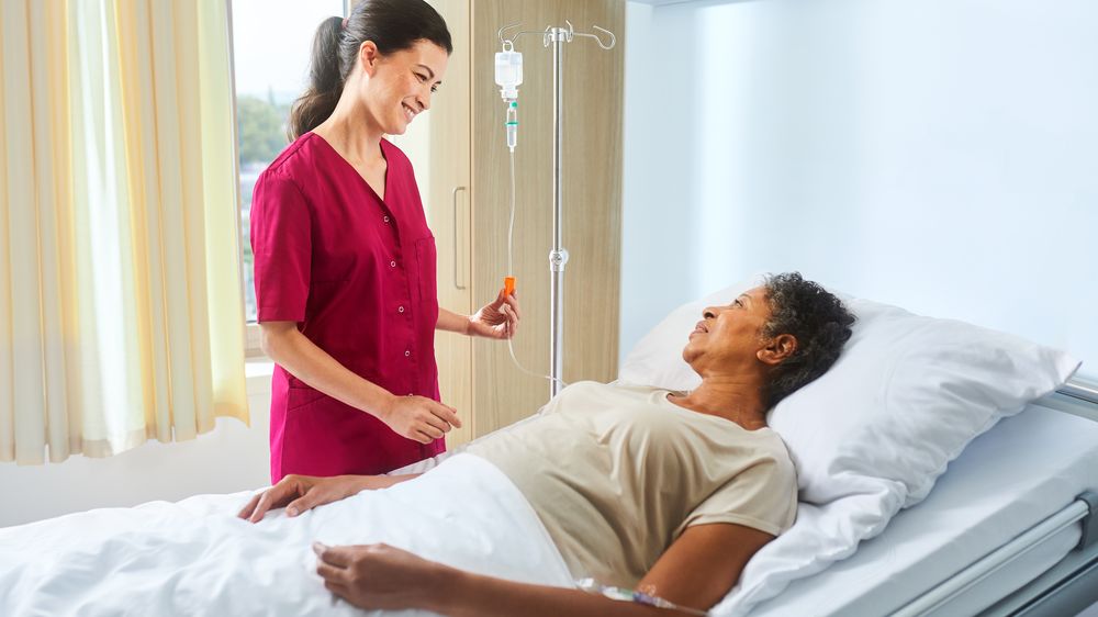 Enfermera con ecoflac plus en un soporte de infusión hablando con un paciente tumbado en la cama